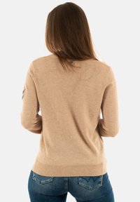 Pull en maille beige avec manches longues, ourlet côtelé et détails aux épaules. Texture douce, design ajusté et finition minimaliste.