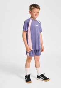 Lila träningsset med kortärmad tröja med rosa detaljer och matchande shorts. Bärs med svarta sneakers och vita crew-strumpor.