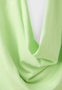 Tissu vert clair avec des plis doux et une texture drapée, montrant un matériau lisse et légèrement brillant en gros plan.