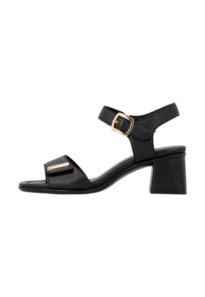 Sandalia negra de cuero con punta abierta, tacón de bloque, correa ajustable en el tobillo con hebilla dorada y adorno rectangular dorado en la correa delantera.