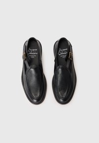 Zwarte leren schoenen met een gestructureerde afwerking. Kenmerken zijn een ronde neus, slingbackriem met een gouden gesp en gestikte randen.