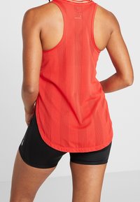 Rode sportieve tanktop met meshpanelen en een gebogen zoom. Gecombineerd met zwarte compressiekorte broek, wat de sportieve uitstraling benadrukt.