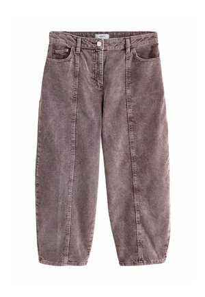 Donna in piedi contro uno sfondo marrone, indossa una polo a maniche corte con fantasia, pantaloni in velluto a coste a vita alta e ballerine viola scuro.