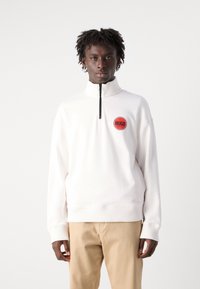 White zip-up sweatshirt made of smooth fabric features a ribbed collar and cuffs, with a circular red logo on the chest and a half-zip front.