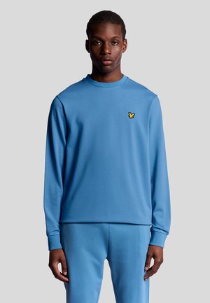 Ljusblå långärmad sweatshirt med rund halsringning och en liten gul logotypaccent på bröstet; mjuk, slät tygtextur.