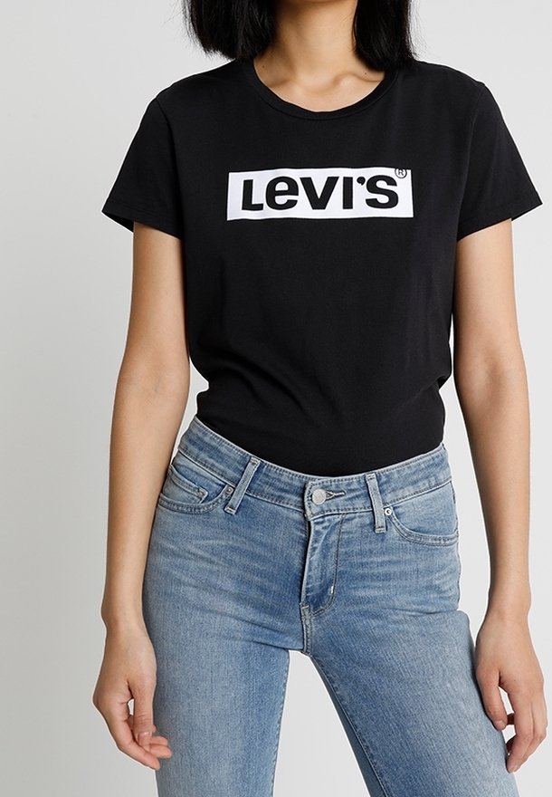 Femme portant un t-shirt noir Levi's et un jean taille haute bleu clair, debout devant un fond uni.
