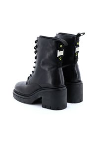 Stivali alla caviglia in pelle nera con tacco spesso, allacciatura frontale e occhielli verde neon; presentano una linguetta sul retro e dettagli in argento.