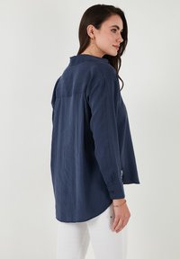 Navy blue long-sleeve shirt with a relaxed fit, pointed collar, buttoned cuffs, and side slits; made from a lightweight, textured fabric.