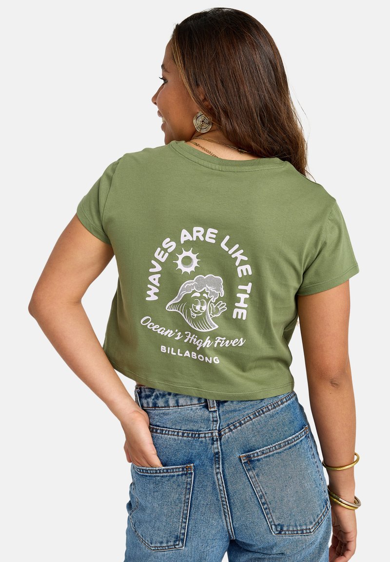 Olive green cropped t-shirt with white graphic text and wave design on the back. Paired with high-waisted blue denim shorts.