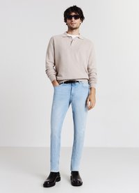 Maglione beige chiaro, jeans slim azzurri, e stivaletti neri. Stile casual con una trama liscia e dettagli minimi. Occhiali da sole scuri.