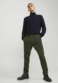 Pulover cu guler înalt, cu dungi, de culoare bleumarin, asortat cu pantaloni subțiri de culoare verde măsliniu și cizme cu șireturi negre, creând o ținută monocromă.