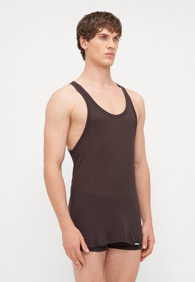 Débardeur marron côtelé avec des bretelles larges, un décolleté en U profond et une silhouette ajustée, porté avec un short foncé assorti. Texture lisse.