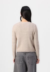 Beige knitted sweater with a textured, ribbed design and long sleeves, paired with high-waisted gray trousers. Features a round neckline.