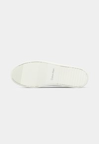 White sneaker sole with textured grip patterns and Calvin Klein logo embossed in the center on a plain light background.