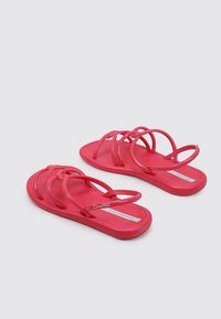Chanclas de goma rosa con múltiples tiras delgadas, una suela plana y un logo en relieve en la plantilla. El diseño es minimalista y casual.