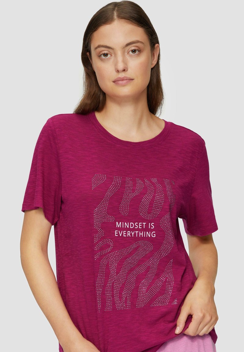 T-shirt fuchsia à manches courtes avec un design texturé comportant la phrase "L'ÉTAT D'ESPRIT EST TOUT" en blanc, ornée d'accents en points.