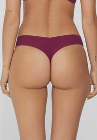Bas de bikini bordeaux au design minimaliste, présente une taille mi-haute et une texture lisse et mate. Aucun motif ni ornement visible.