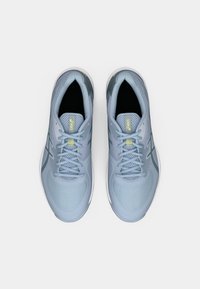 Lys blå sportsko med mesh-overdel, med kontrasterende grønne detaljer, polstret såle og flate lisser. Har logo på tungen og siden.
