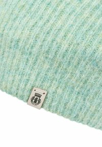 Soft textured light blue knit wool fabric with a small beige tag displaying a black emblem stitched near the edge.