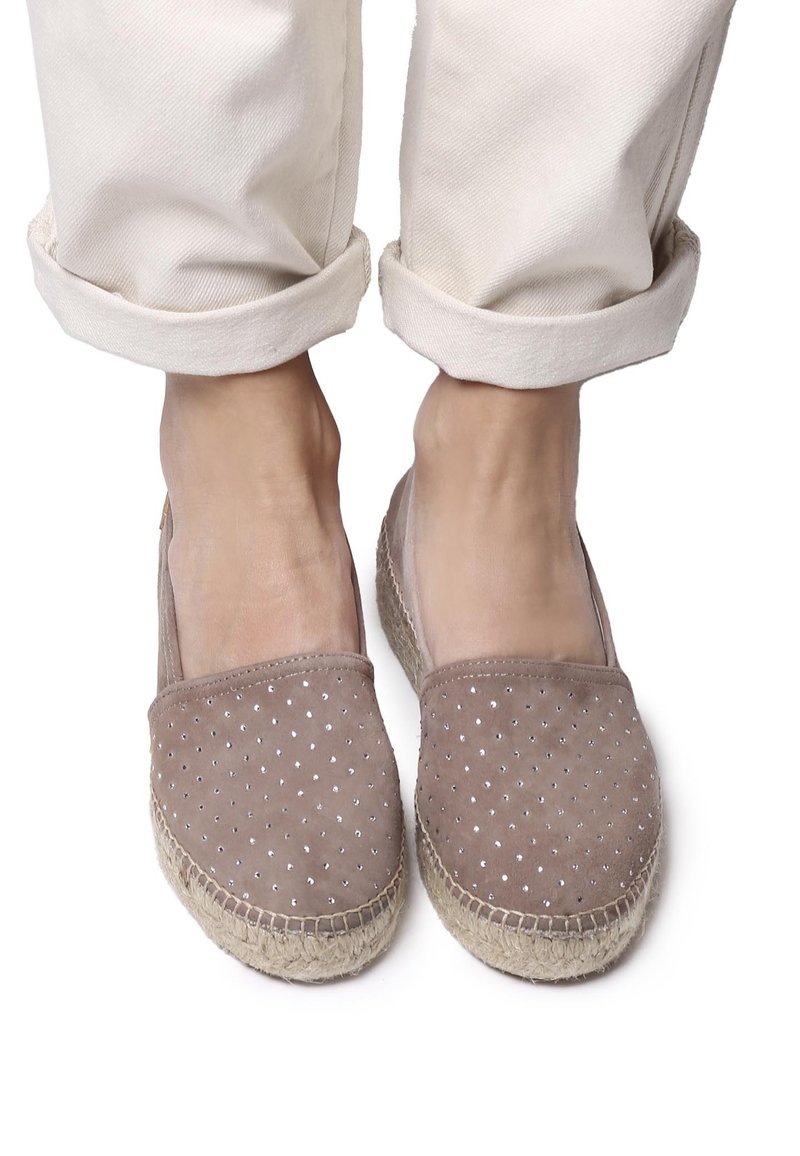 Espadrillas in suede beige con un motivo a diamante di piccoli chiodini metallici, suola avvolta in juta e aperture laterali, indossate con pantaloni crema arrotolati.