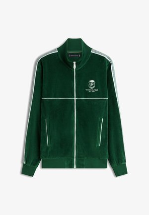 Donkergroene velours jas met ritssluiting, witte strepen op de mouwen, witte biezen en het Tommy Hilfiger-logo op de borst.