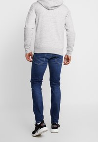 Felpa con cappuccio grigia con finitura strutturata, abbinata a jeans slim fit blu scuro e sneaker nere con suola bianca e dettaglio rosso.