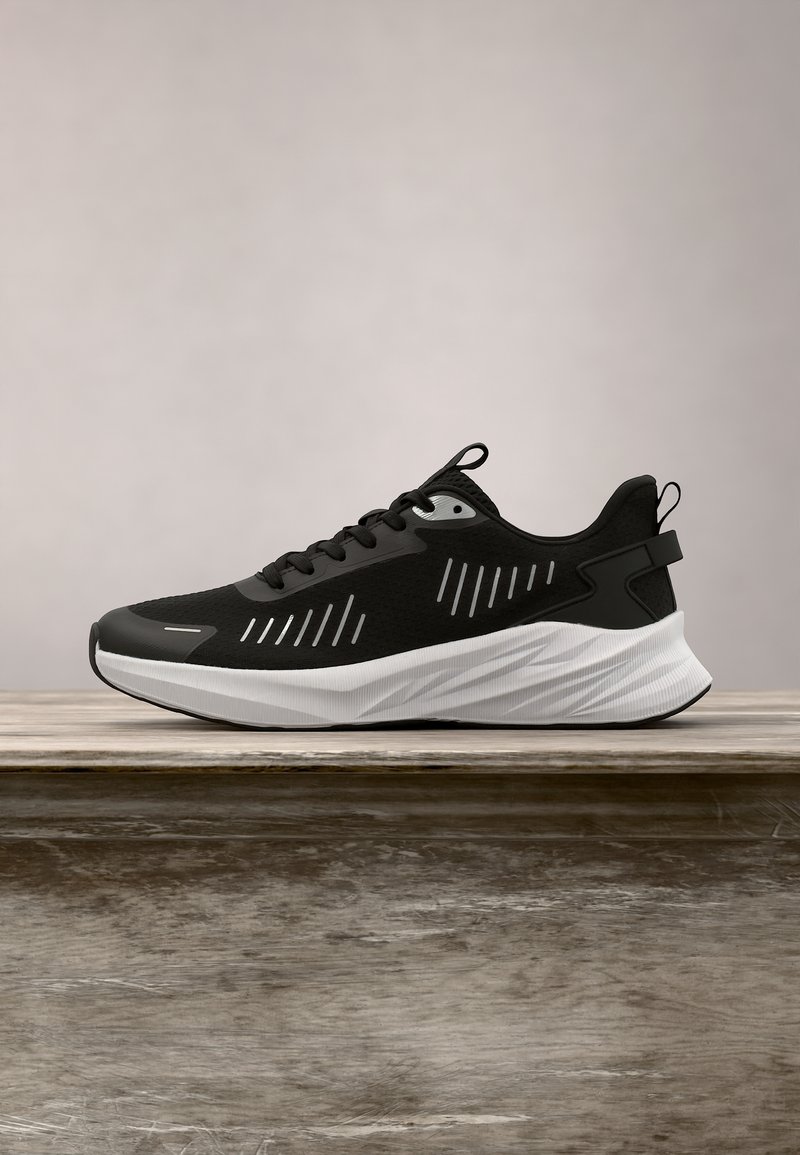 Baskets de sport noires avec semelle blanche et accents argentés réfléchissants, exposées sur une surface en bois sur fond gris uni.