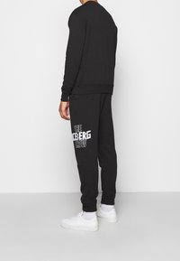 Pantaloni della tuta neri e felpa coordinata con collo rotondo, in misto cotone, con grande scritta bianca "THE ICEBERG CREW" sui pantaloni. Sneakers bianche.