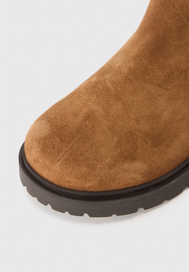 Primo piano di una punta di stivale in suede marrone con una robusta suola in gomma nera e un motivo di battistrada aggressivo.