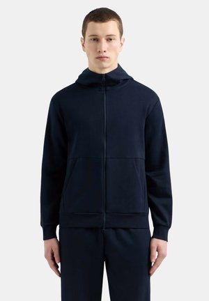 Marinblå zip-up hoodie i mjukt material med en känguruficka, huva och ribbade ärmslut. Minimalistisk design, slät textur.