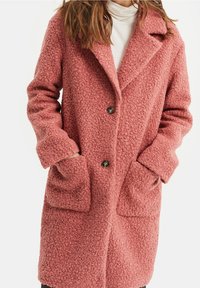 Abrigo suave rosa, texturizado, con cuello, dos grandes bolsillos frontales y tres botones. Hecho de una tela cálida, tiene un corte holgado.