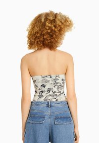 Top sin tirantes en color crema con patrones de dragón negro y flores; combinado con pantalones cortos de mezclilla de talle alto con bolsillos de solapa.