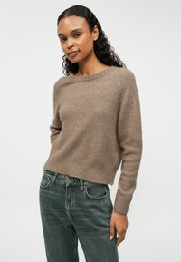 Bruine gebreide trui met een brede halslijn en lange mouwen, gecombineerd met iets te grote blauwe jeans. Zachte textuur opgemerkt.