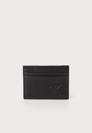 Porte-cartes en cuir noir avec quatre emplacements, logo en relief et texture lisse. Design minimaliste avec des accents cousus le long des bords.