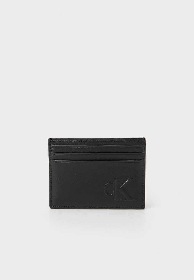 Cardholder din piele neagră, cu patru sloturi, logo în relief și textură netedă. Design minimalistic cu accente cusute de-a lungul marginilor.