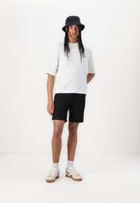 White cotton t-shirt, short sleeves; black shorts; dark blue bucket hat; beige sneakers with brown soles; light gray socks.