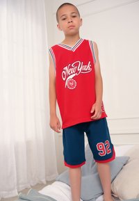 Red basketball jersey featuring "New York" in white script, paired with blue mesh shorts with a red hem and number "92" on the side.