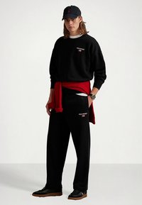 Μαύρο φούτερ με το λογότυπο "Polo Sport", κόκκινο πουλόβερ δεμένο στη μέση, μαύρο παντελόνι και μαύρο καπέλο. Μαλακό ύφασμα, άνετη εφαρμογή και αθλητικά παπούτσια.