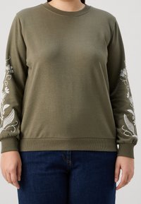 Felpa verde oliva in cotone, con ricami floreali bianchi intricati sulle maniche e orlo e polsini a costine.