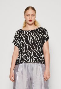 Haut à rayures noir et blanc avec une coupe ample, des manches courtes et un décolleté large, associé à un pantalon argenté brillant.