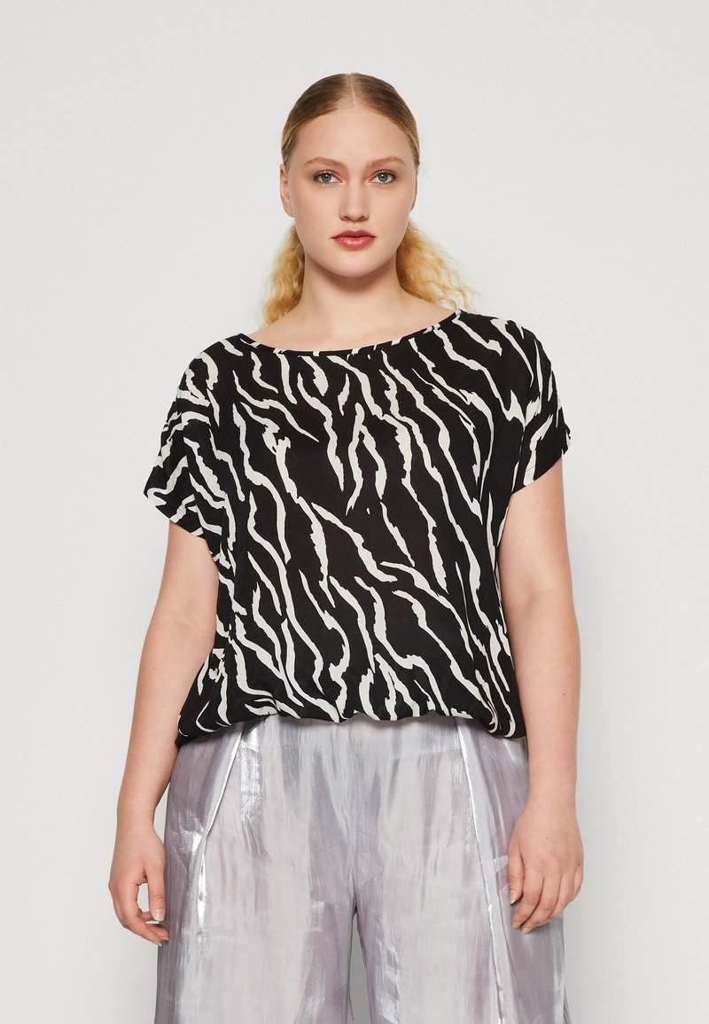 Haut à rayures noir et blanc avec une coupe ample, des manches courtes et un décolleté large, associé à un pantalon argenté brillant.