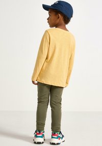 Langærmet gul skjorte, grønne leggings og multikolore sneakers. Skjorten har en rund halsudskæring, afslappet pasform og blød tekstur.