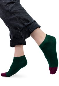 Zielona skarpetka do kostki z bordowym palcem. Miękka, dziana faktura. Noszona z podwiniętymi ciemnymi dżinsami, odsłaniająca kostkę i stopę.
