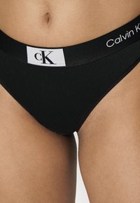 Perizoma nero Calvin Klein con una fascia larga decorata con accenti bianchi del logo e una texture liscia. Il design enfatizza la semplicità e il comfort.