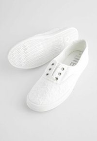 Weiße Spitzen-Schlupfschuhe mit Gummisohlen, ausgestattet mit sechs Ösen und einem strukturierten Blumenmuster auf dem Obermaterial.