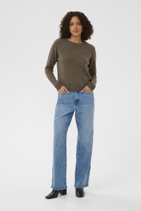 Pull marron en maille avec encolure ronde, associé à un jean bleu clair ample avec des boutons visibles sur les côtés et des bottes à talons noires.