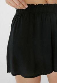 Shorts noirs avec une taille élastiquée et volantr. Fabriqués en tissu léger, ils ont une texture lisse et un ourlet incurvé en bas.