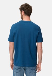 Blue short-sleeve T-shirt in a solid color, made of cotton, featuring a round neckline and a smooth texture. Worn with light denim jeans.