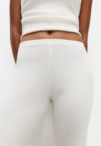 Leggings blancs en maille côtelée avec une taille élastique et une finition texturée, épousant étroitement le corps sans motifs visibles.