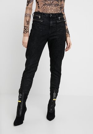 Zwarte denim broek met een getextureerde afwerking, voorzien van ritszakken en contrasterende ritsen bij de enkels. Strak aansluitend ontwerp.